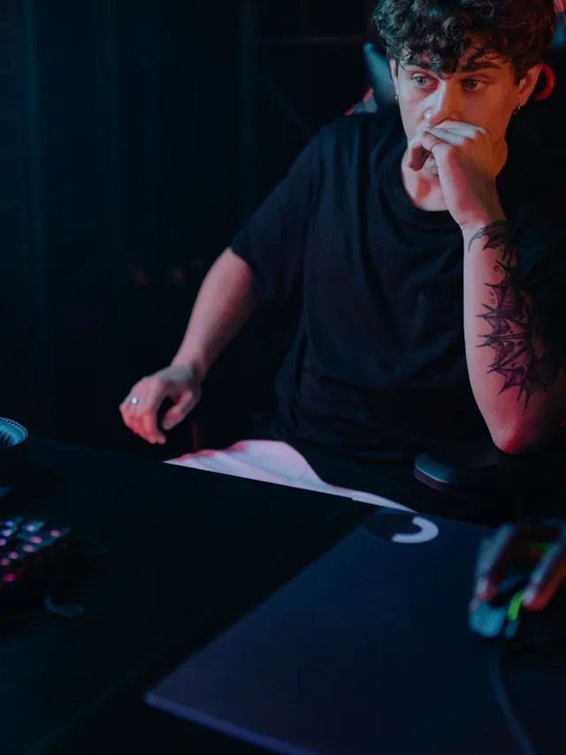 Gamer with a tattooed forearm resting his chin on his hand while studying his monitor, mouse under his other hand
