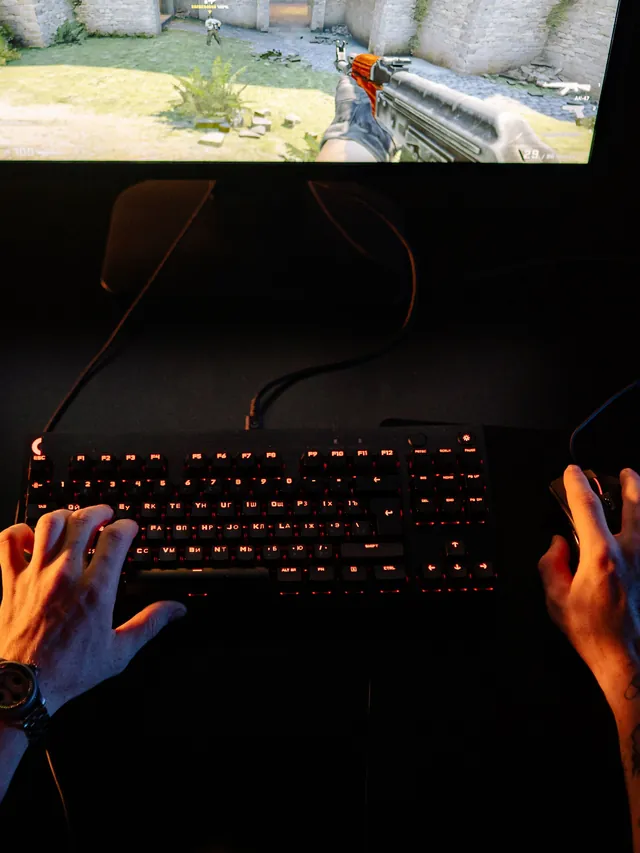 Overhead view of a player’s hands on a backlit keyboard and a wired mouse during a shooter match