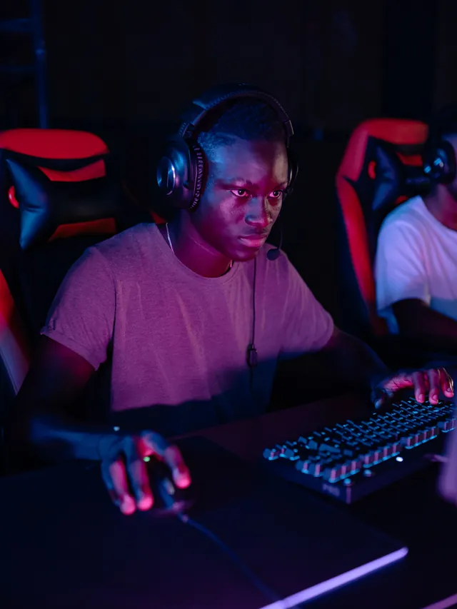 Focused gamer in a headset gripping a mouse mid-match in a red-lit esports room