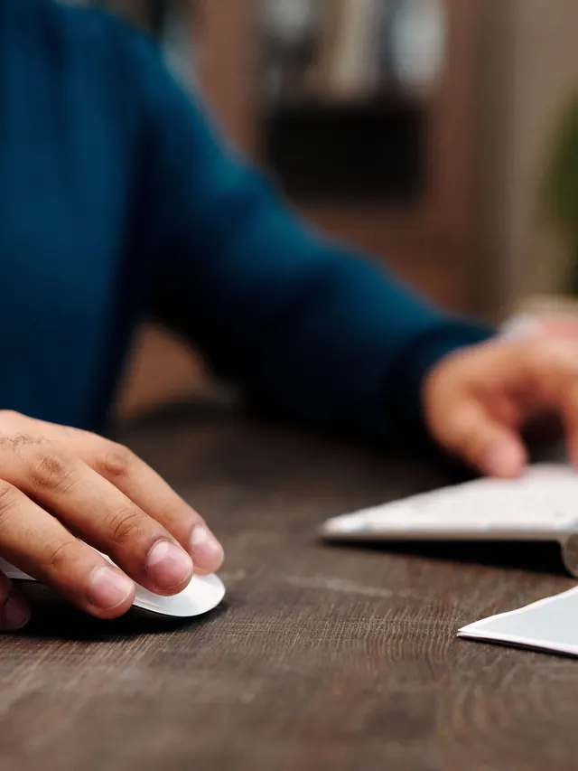 Hand using a generic mouse beside a keyboard; illustrative photo