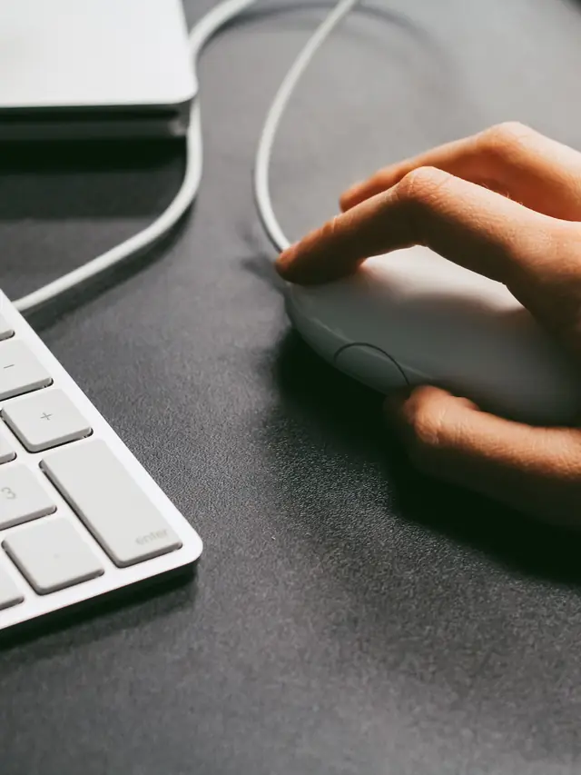 Hand using a generic computer mouse beside a keyboard; illustrative photo