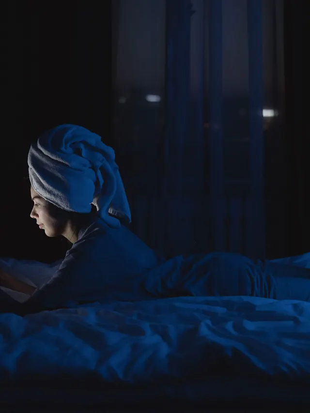 Woman using a smartphone in a dark bedroom lit by the screen