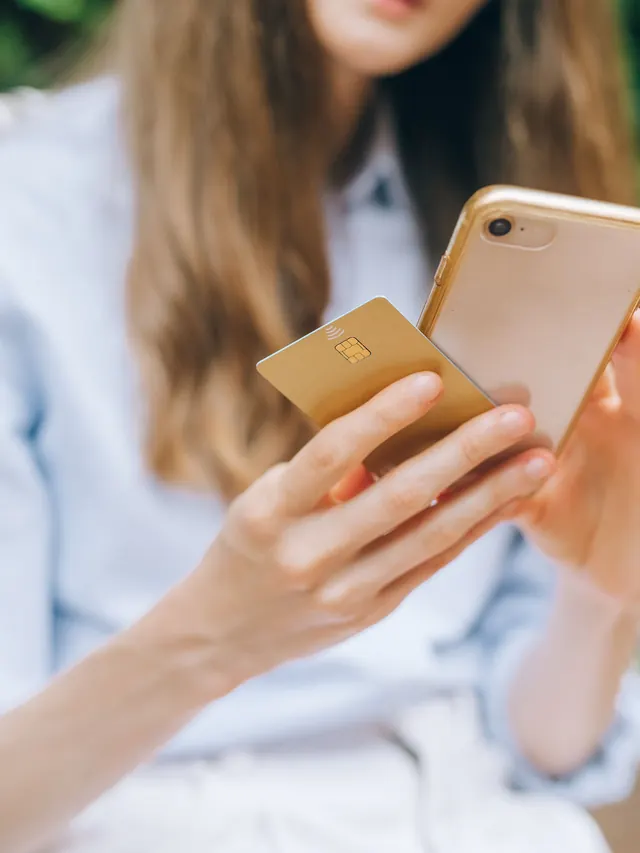 Woman holding a smartphone and payment card while making a purchase decision