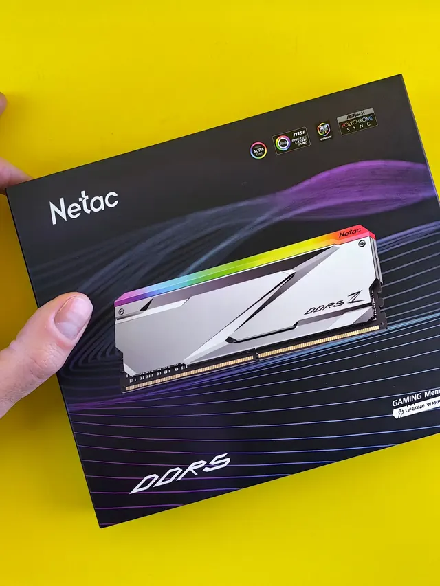 Hand holding a boxed DDR5 gaming memory kit against a yellow background