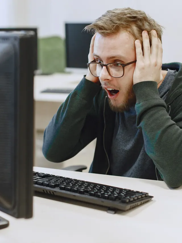 Shocked man in eyeglasses staring at a computer monitor in an office