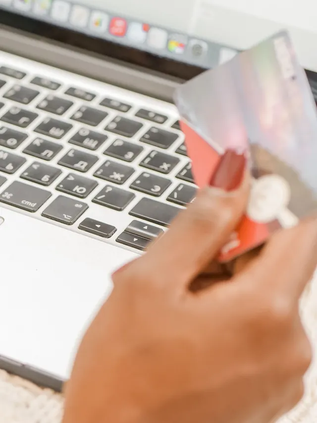 Hand holding payment cards over a laptop during an online checkout