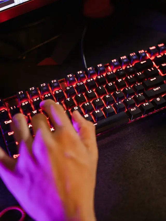 Hand pressing keys on a red-backlit gaming keyboard