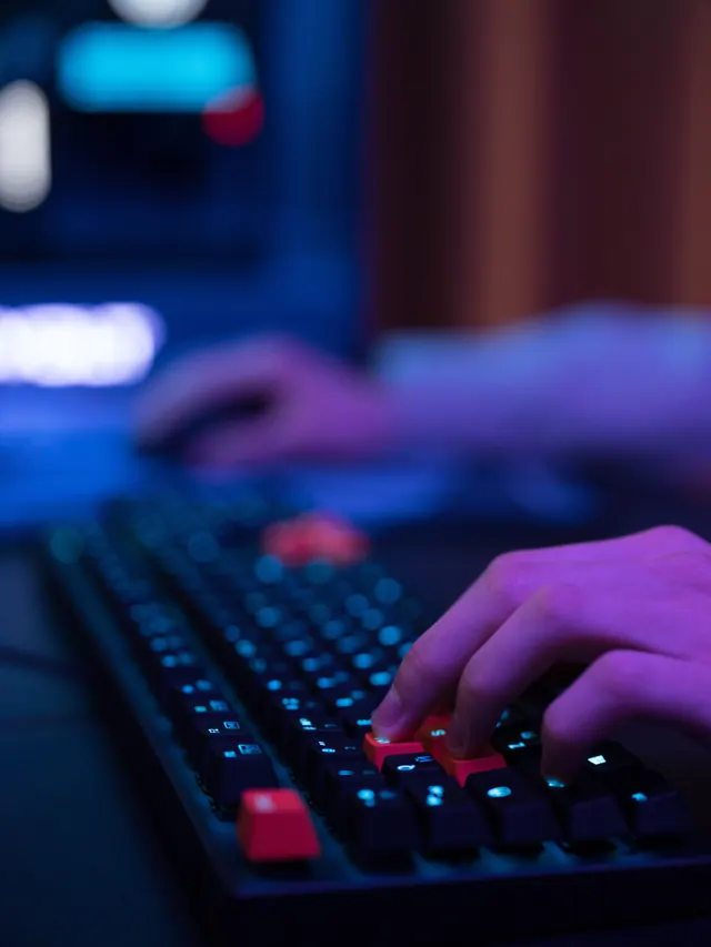 Hands typing on an RGB keyboard in a dark gaming setup; illustrative stock photo
