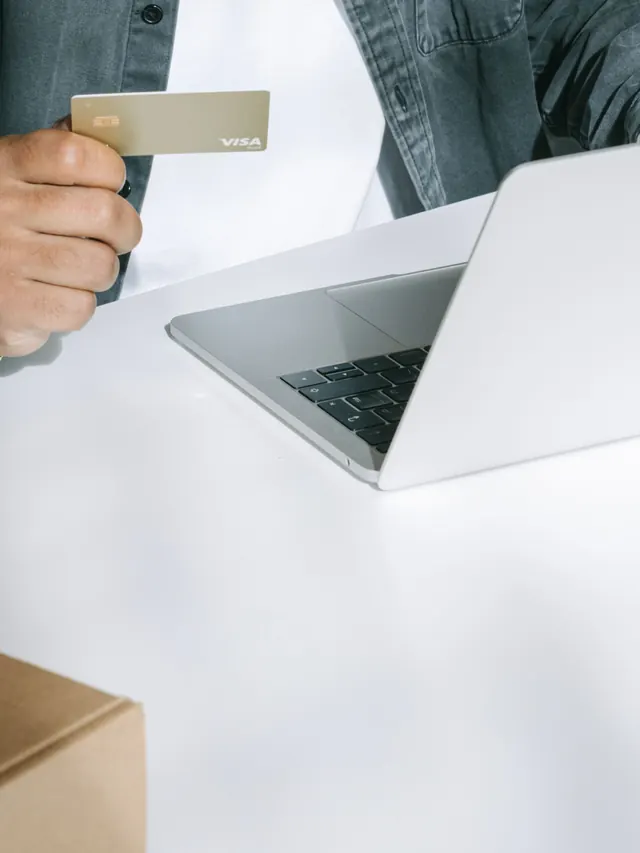 Person holding a payment card while shopping on a laptop; illustrative stock photo