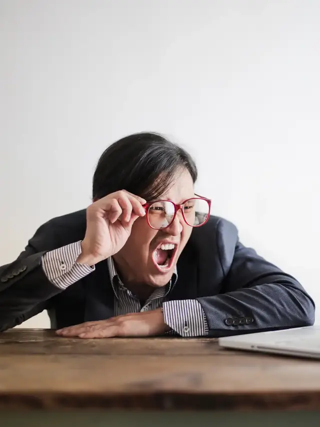 Woman in glasses reacting to a laptop problem at a desk