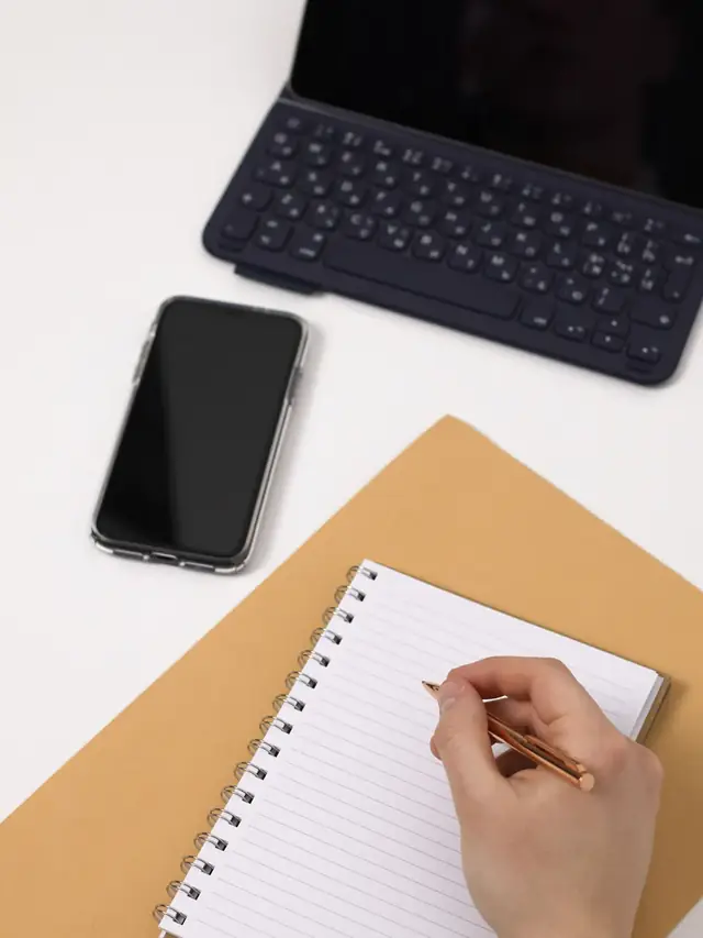 A hand writing in a notebook beside a keyboard and phone; stock illustration of making a binding plan