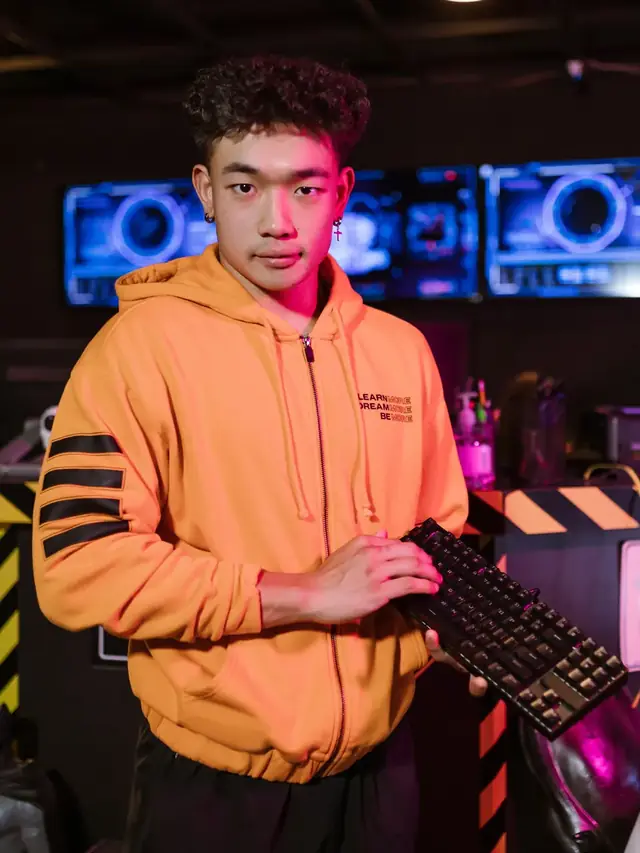 A man in an orange hoodie holding a generic keyboard; illustrative stock, not a Tartarus device or an endorsement