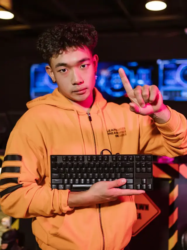 The same orange-hoodie gamer holding a generic keyboard and raising a finger; illustrative stock for checking the exact model