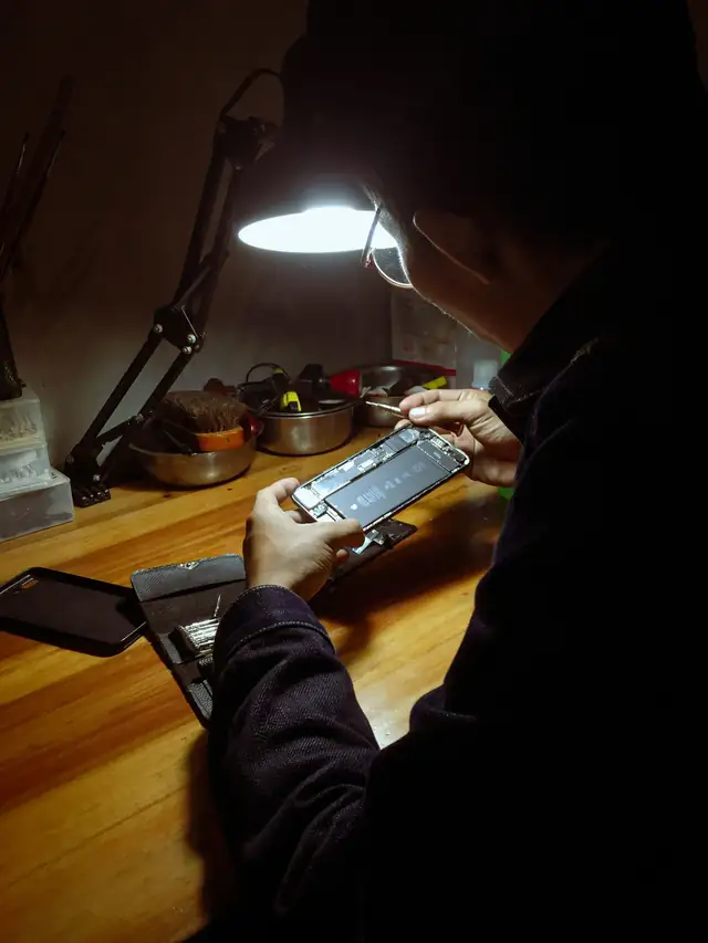 Man repairing an opened smartphone under a desk lamp