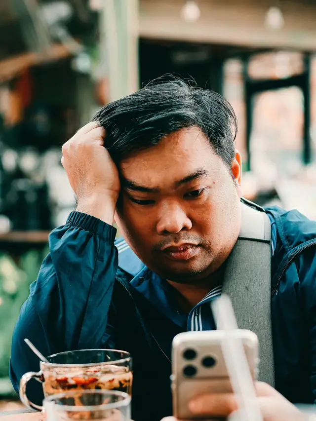 Man checking his phone in a cafe looking unconvinced