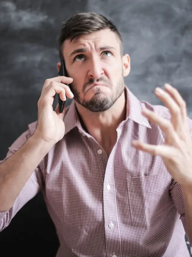 Man in a pink shirt looking stressed while talking on a smartphone