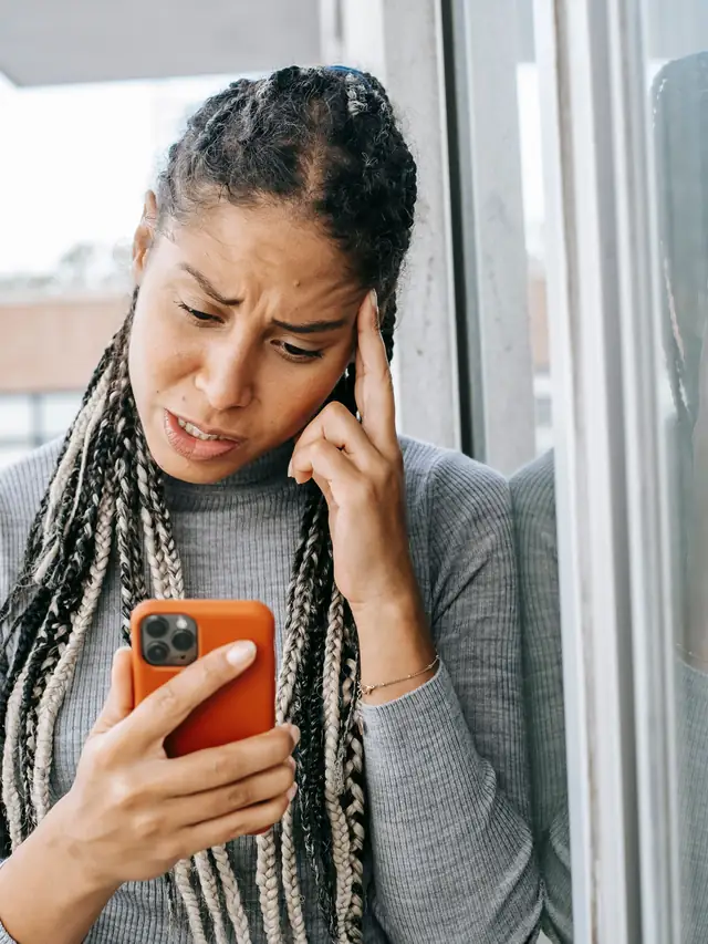 Woman on a balcony looking dissatisfied at her phone screen