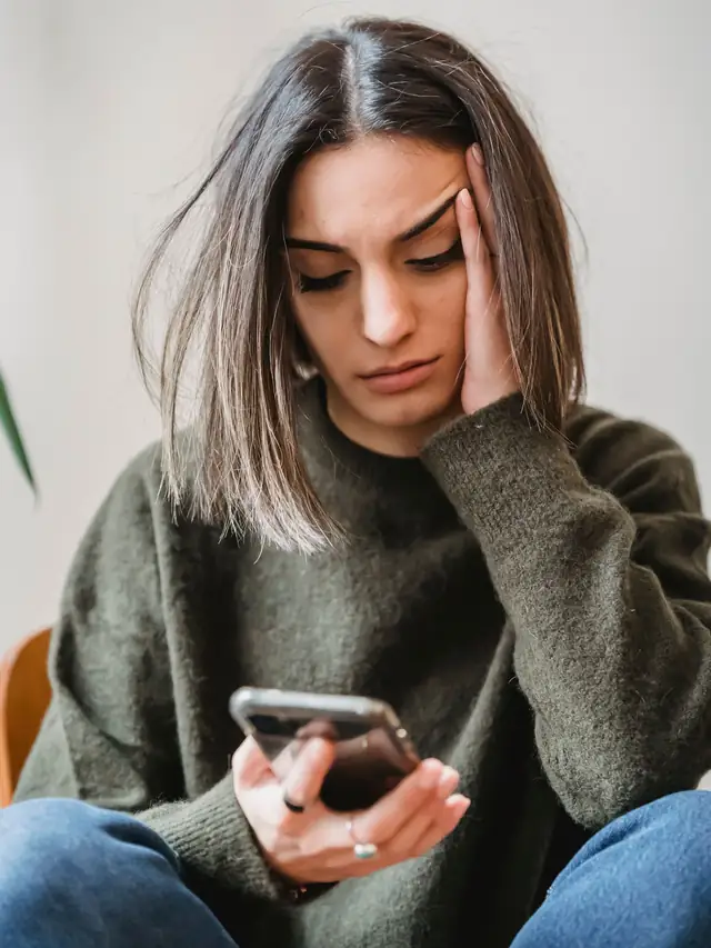 Young woman indoors looking concerned while reading her smartphone
