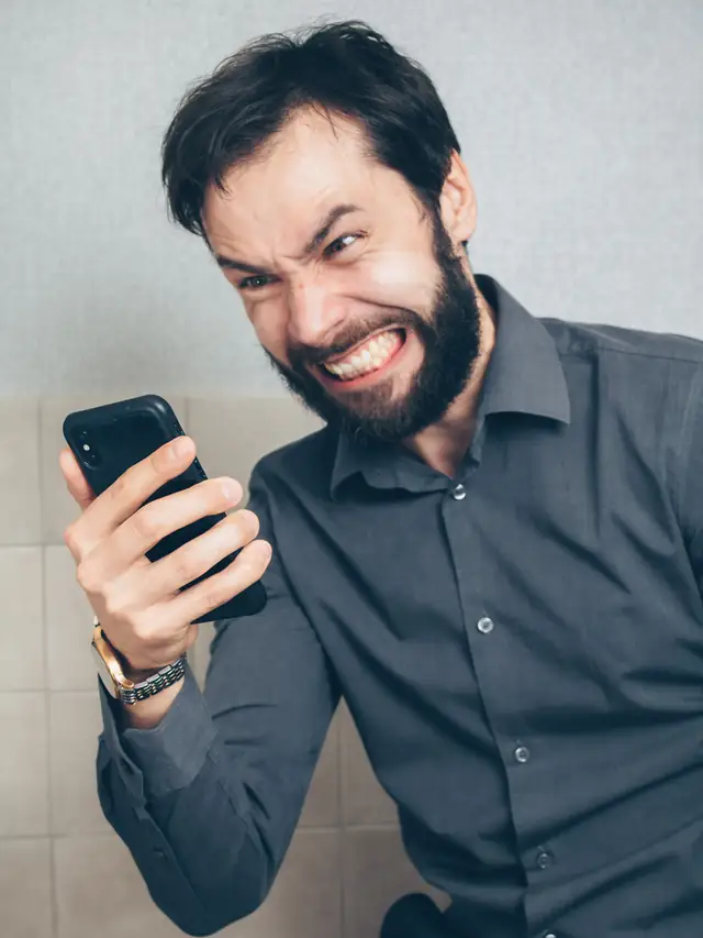 Man looking frustrated while holding a smartphone in an office
