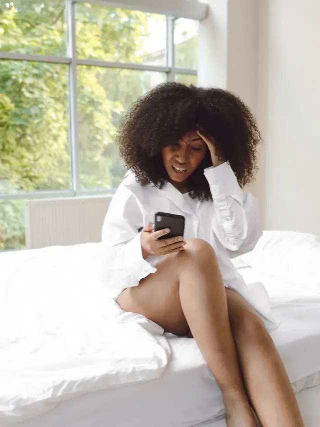Woman with curly hair checking settings on her smartphone indoors