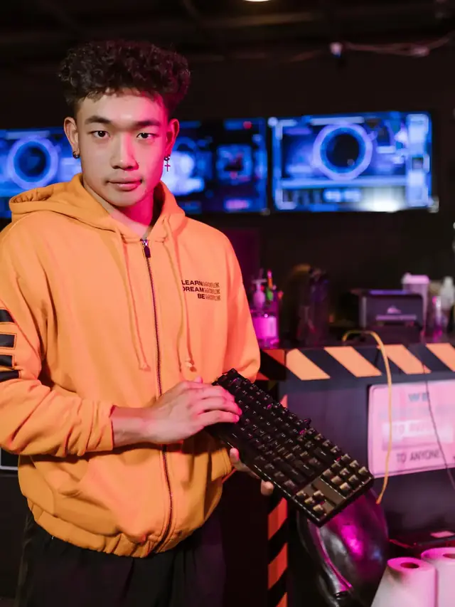 A man in an orange hoodie holding a generic mechanical keyboard in a gaming venue; illustrative stock, not a Wooting product